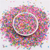 A bowl filled with colorful polymer clay slice sprinkles scattered on a white surface.