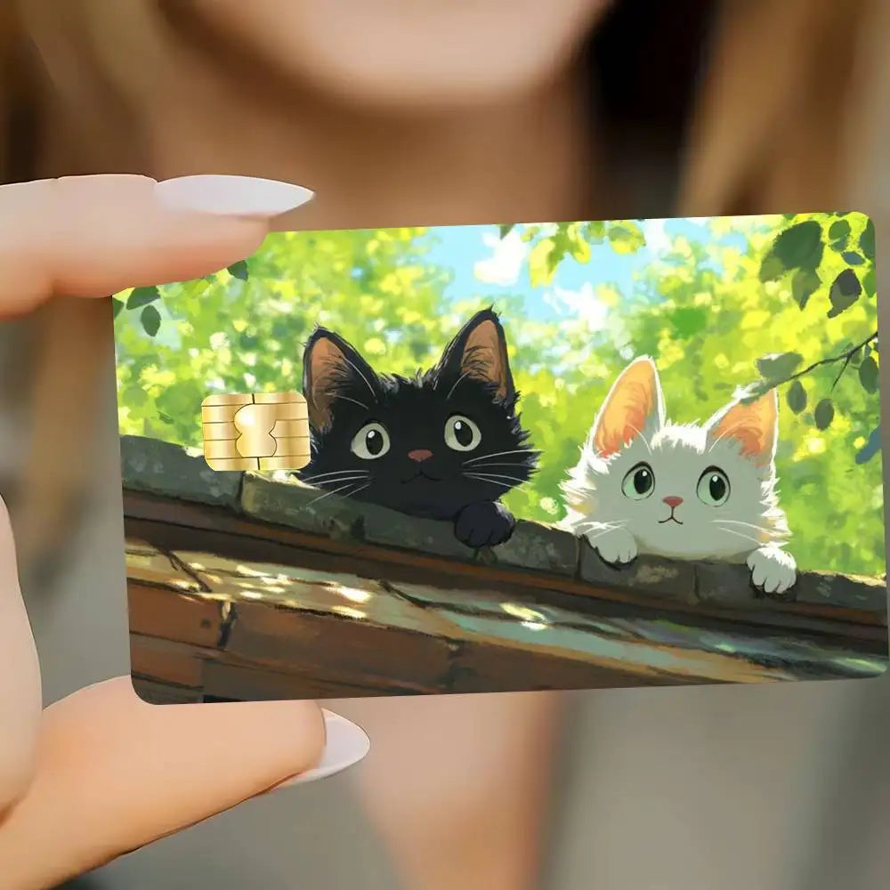 A hand holds a card featuring cute black and orange cats sitting on a wooden ledge with gold coins.