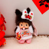 A cute Monchhichi plush keychain with black and white fur, pink clothing, and an elaborate headpiece.