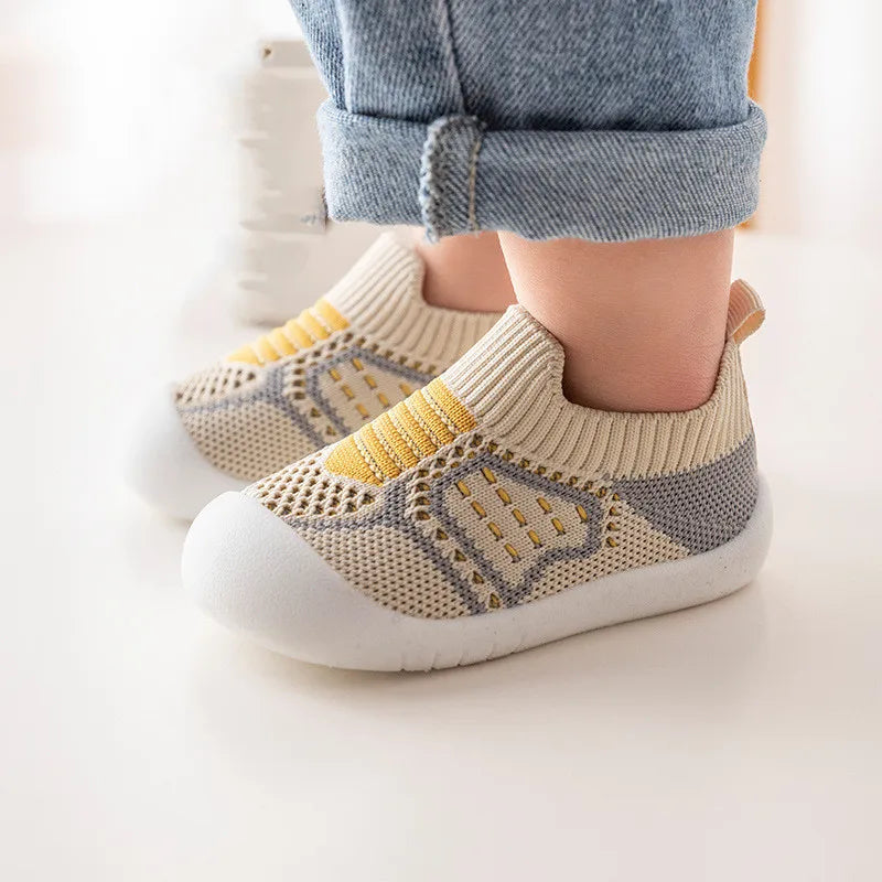 A pair of beige and yellow breathable anti-slip baby first walker shoes worn by a child.