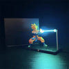 A figurine of Son Goku performing a Kamehameha pose illuminated by a bright blue LED light on a desk.