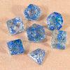 A collection of translucent blue glitter polyhedral dice including a D4, D6, D8, D10, D12, and D20 scattered on a pink surfac