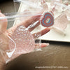 A hand holds a clear plastic bag containing a pink glitter squishy fidget toy and a necklace with a heart pendant.