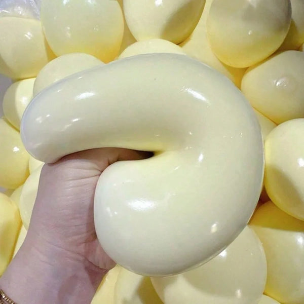 A hand is squeezing a large, smooth, pale yellow sensory stress relief squishy fidget ball surrounded by many similar balls.