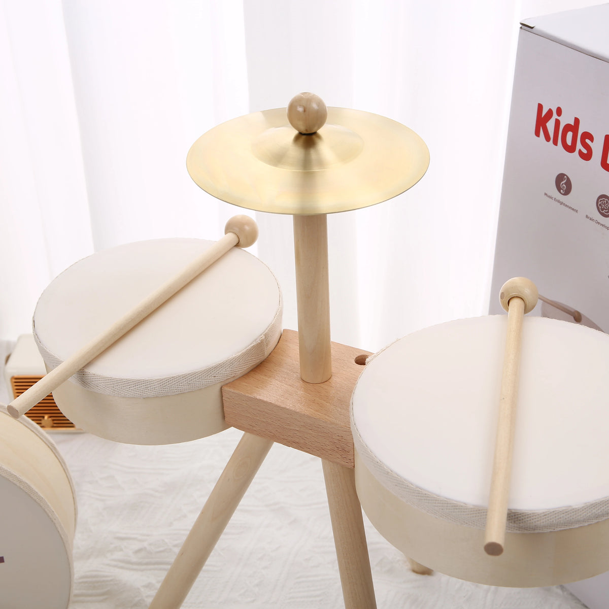 A wooden kids drum set with two drums and a mallet displayed on a light-colored surface.
