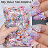 A hand holds a small plastic bag filled with 50 grams of multicolor resin nail charms for crafting.