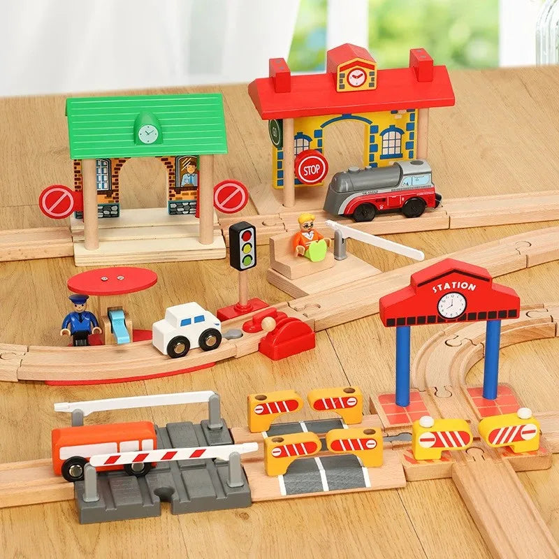 A wooden train track accessory set featuring a red and yellow train station, a red house, and various train vehicles.