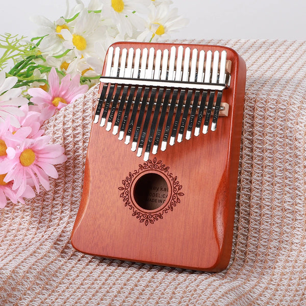 A wooden kalimba finger piano with metal tines rests on a knitted fabric next to some flowers.