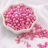 A pile of assorted pink and magenta pearl beads in a white dish and scattered on a white cloth.