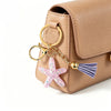 A tan leather pouch with a gold ring and a starfish beaded keychain attached.