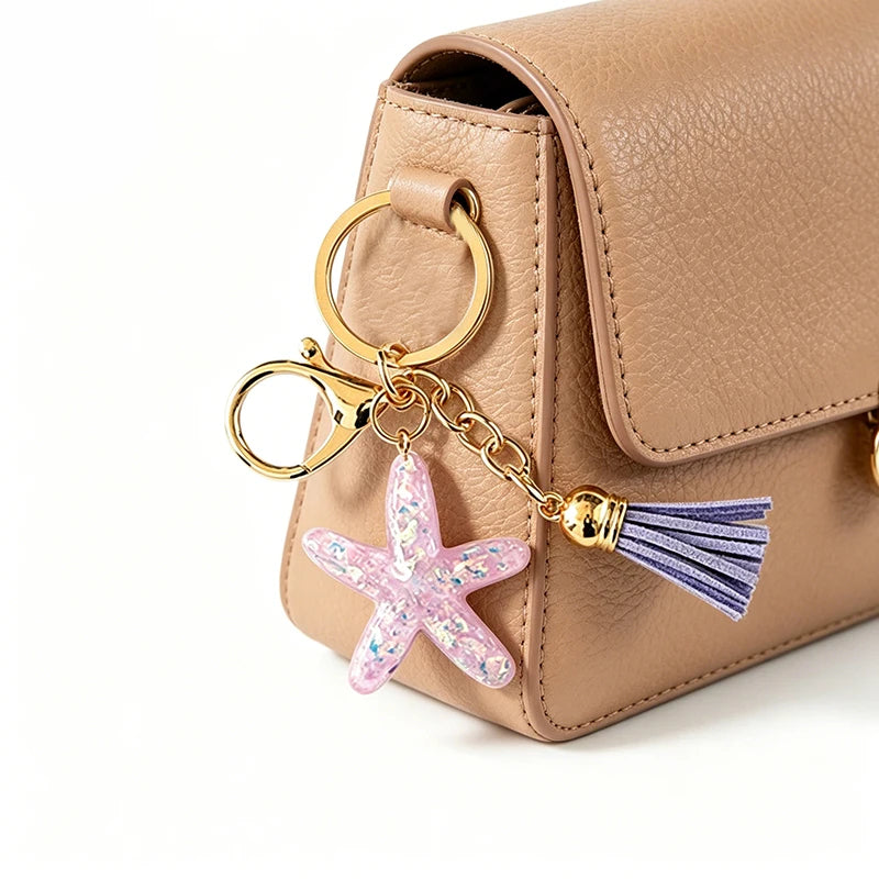A tan leather pouch with a gold ring and a starfish beaded keychain attached.