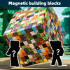 Un grand cube coloré de blocs magnétiques sur une surface en bois avec deux silhouettes à proximité.