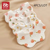 A set of four white baby bandana bibs with pink and yellow fruit patterns laid out on a beige background.