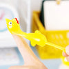 A hand holds a yellow, bird-shaped catapult toy with a red beak and eye.
