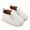 A pair of white baby first walker sneakers with a dinosaur print detail and brown lining.
