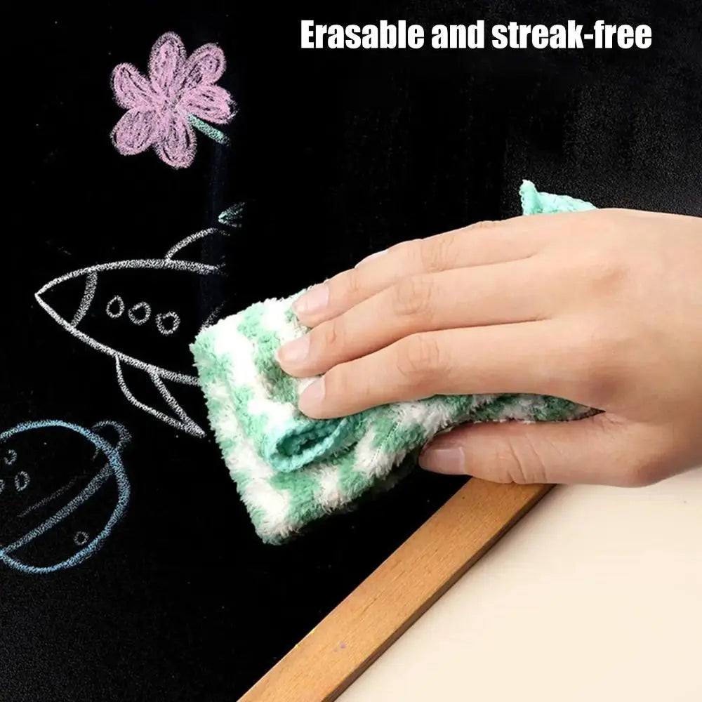 A hand is using a green, fuzzy eraser to clean white chalk drawings on a black chalkboard.
