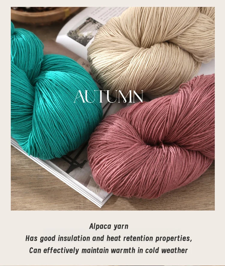 Three skeins of alpaca yarn in teal, beige, and dusty rose colors are displayed on a wooden surface.