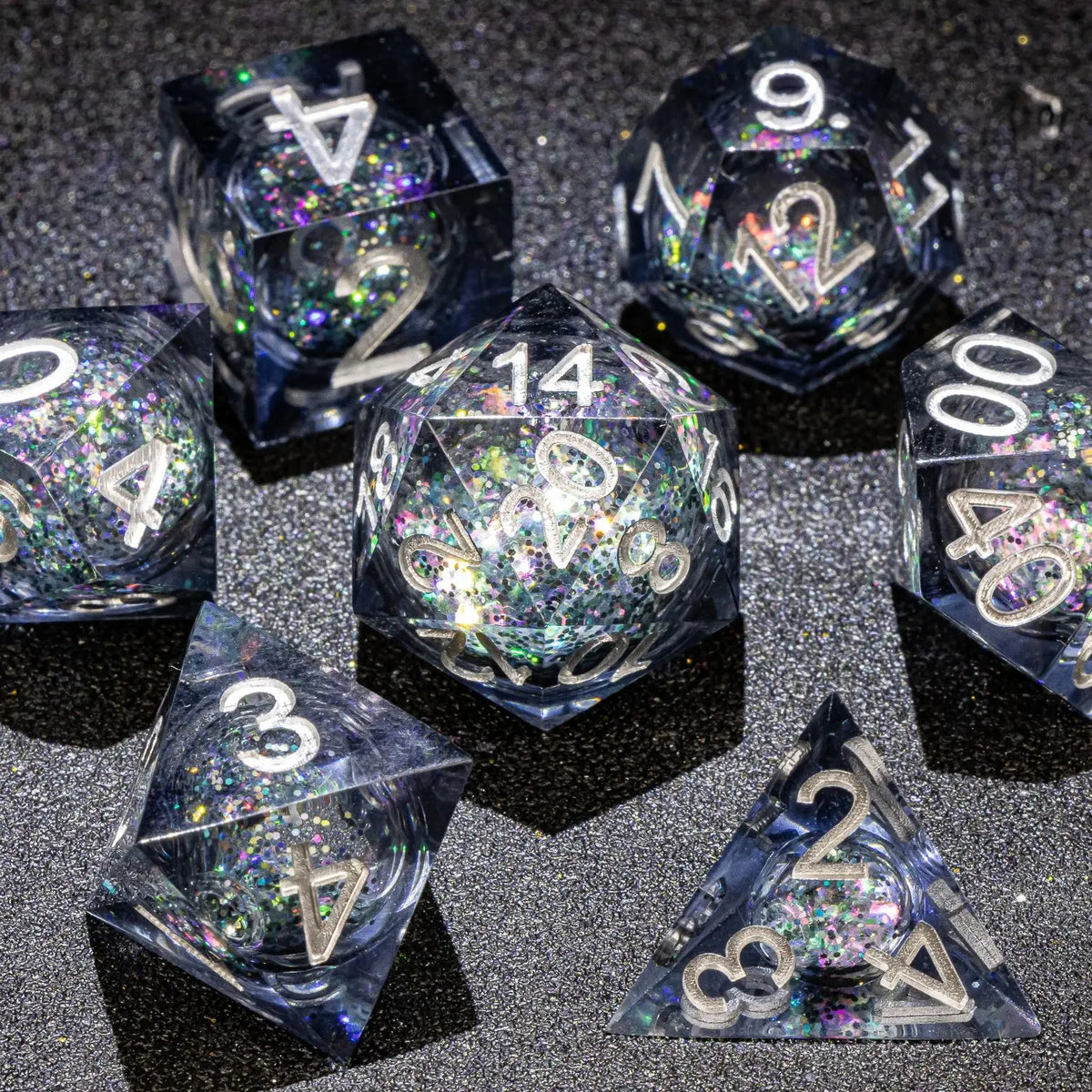 A collection of polyhedral dice, including d4, d6, d8, d10, d12, and d20, with a galaxy finish, scattered on a dark surface.