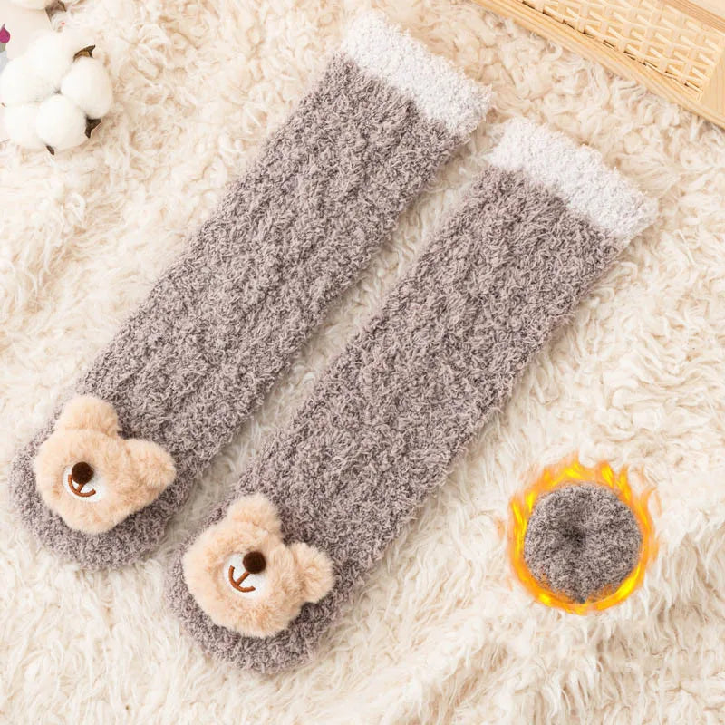 Gray plush baby knee-high socks with white trim lying on a fluffy white surface.