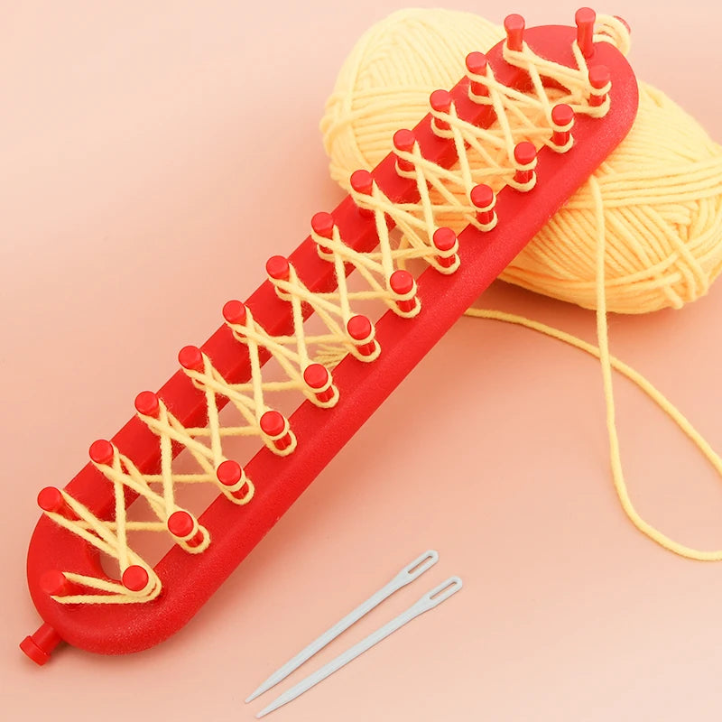 A red knitting loom with crochet hooks and a ball of yellow yarn is shown on a pink background.