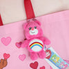 A pink Care Bears plush keychain charm with a rainbow design attached to a pink fabric bag.