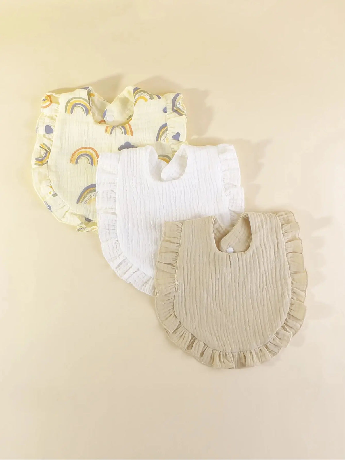 A set of three pure cotton muslin baby bibs featuring yellow and white fabric with rainbow designs.