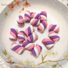 A collection of pink and purple striped polymer clay marshmallow charms arranged on a white plate.