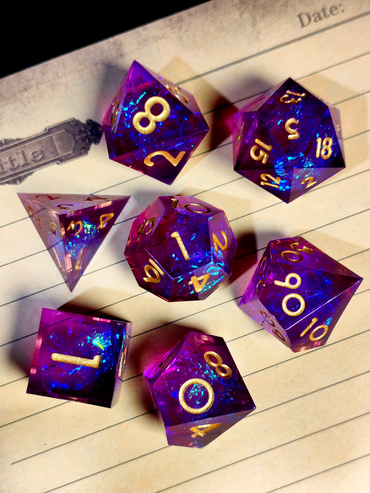 A collection of handcrafted resin polyhedral dice in light purple with gold numbers scattered on lined paper.