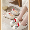 A close-up of a pair of white plush non-slip indoor slippers with red and orange accents resting on a light beige rug.