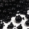 A close-up view of small, round black imitation pearl beads scattered on a white surface.