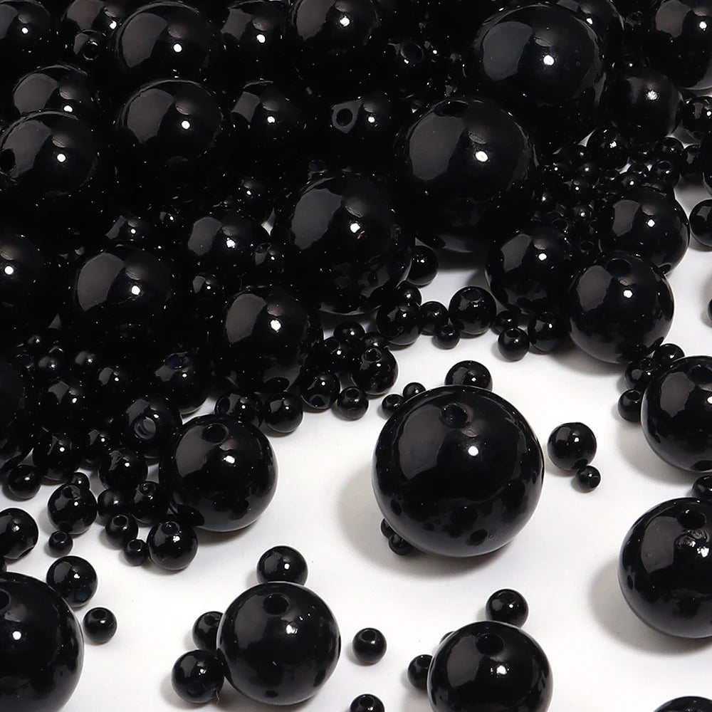 A close-up view of small, round black imitation pearl beads scattered on a white surface.