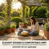A young girl is playing a golden handpan drum with wooden mallets in a garden setting.