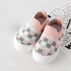 A pair of pink and gray plaid slip-on toddler shoes for first walkers resting on a white surface.