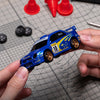 A blue 1:43 scale RC drift car is held above a graph paper, showcasing its realistic body shell and features.
