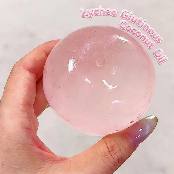 Une main tient une balle anti-stress en huile de coco rose et transparente sur un fond clair.