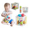 A toddler is playing with a wooden Montessori shape sorter cube featuring various colored fruit and vegetable shapes.