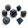 A set of premium metal polyhedral dice with a dark finish and multicolor gold accents scattered on a white background.