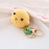 A yellow crocheted fruit keychain pendant with black eyes and a green charm on a white background.