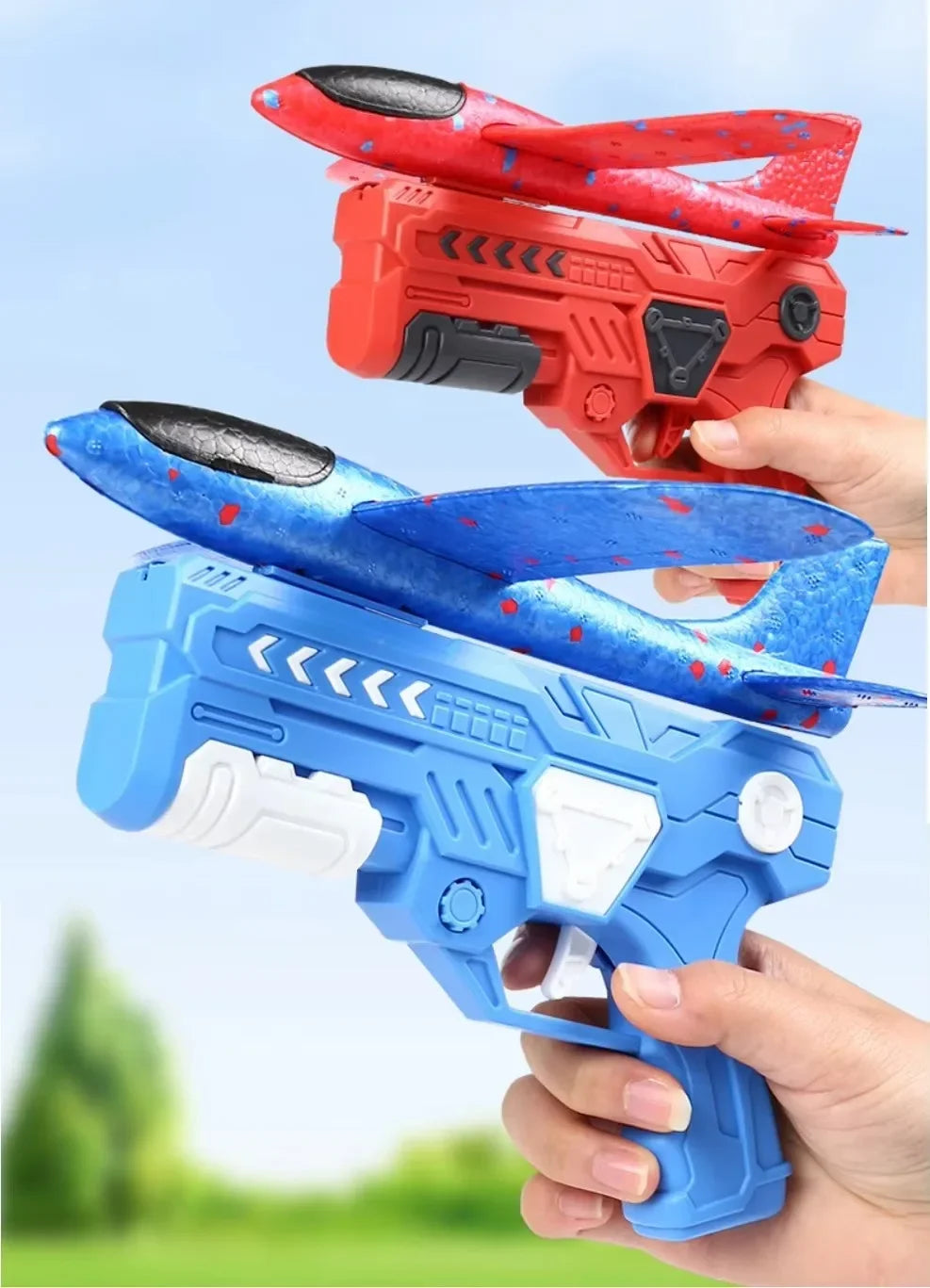 Deux lanceurs d'avions en mousse, un rouge et un bleu, sont tenus par des mains sur un fond de ciel bleu clair.
