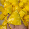 A hand holds a bright yellow cheese ball stress relief squeeze toy surrounded by other yellow balls.