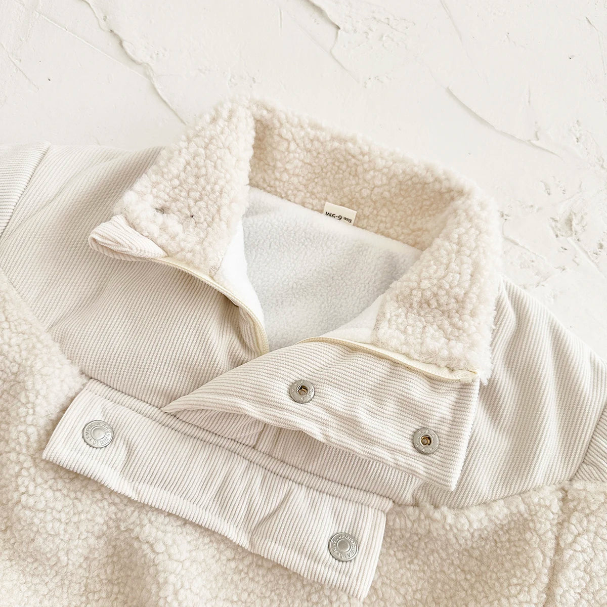 A close-up of a cream fleece-lined winter coat with a textured collar and half-zip closure.