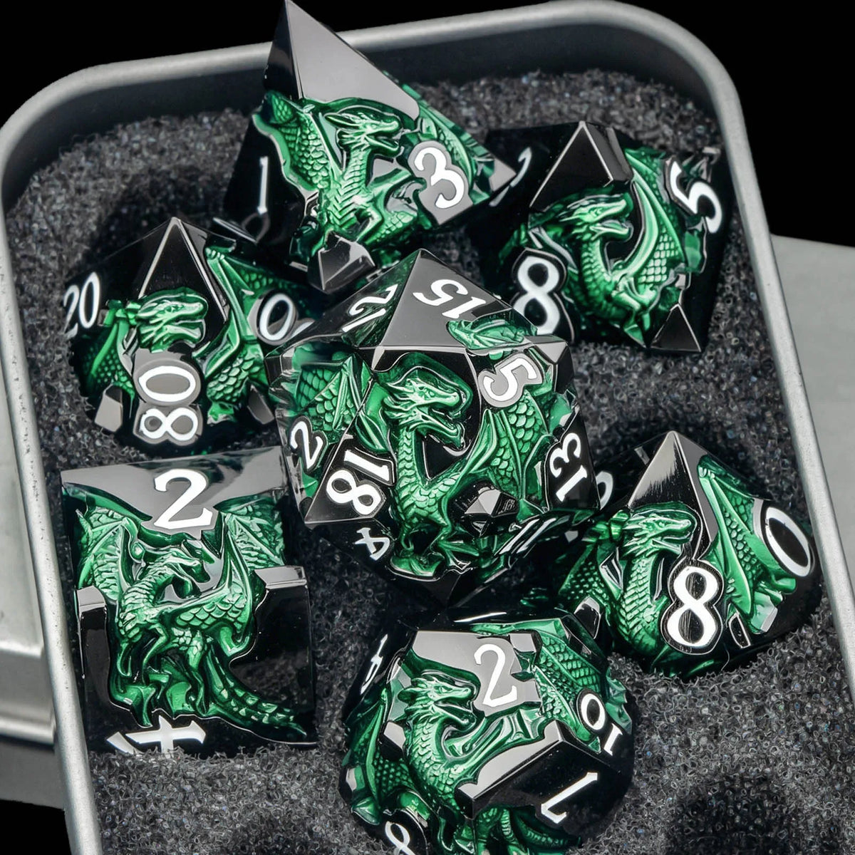 A set of black metal dice featuring a green dragon design displayed in a gray container.