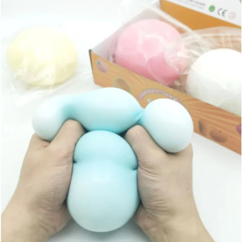 Hands holding a light blue giant squishy stress ball next to other squishies in a box.