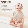 A smiling baby wearing a pink bow and a light pink muslin bib on a white blanket.