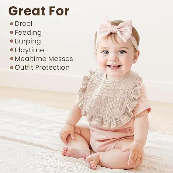 A smiling baby wearing a pink bow and a light pink muslin bib on a white blanket.
