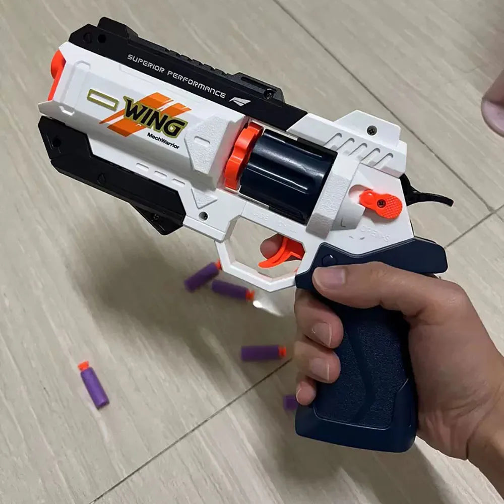 A hand holds a white and black foam bullet toy pistol with an orange barrel and a yellow logo on it.