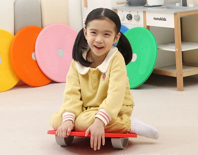 A young girl is sitting on a red balance stepping stone toy with various colored plastic stones in the background.