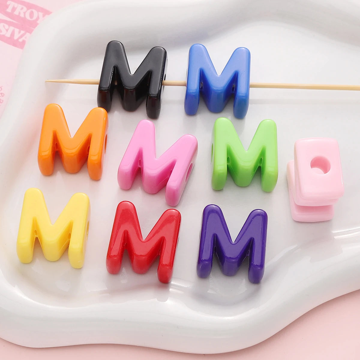 A collection of colorful acrylic letter beads in various shades of black, blue, orange, pink, green, and purple arranged on a