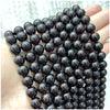 A hand holds a string of dark, polished natural stone beads for DIY jewelry making.
