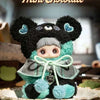 A cute black and teal plush charm of a bear with large eyes sitting on a white plate.
